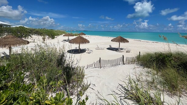 A beach with thatched umbrellas, lounge chairs, and a wooden fence. - The Green Grouper, oversized beach villa. (Central Abaco , Treasure Cay)