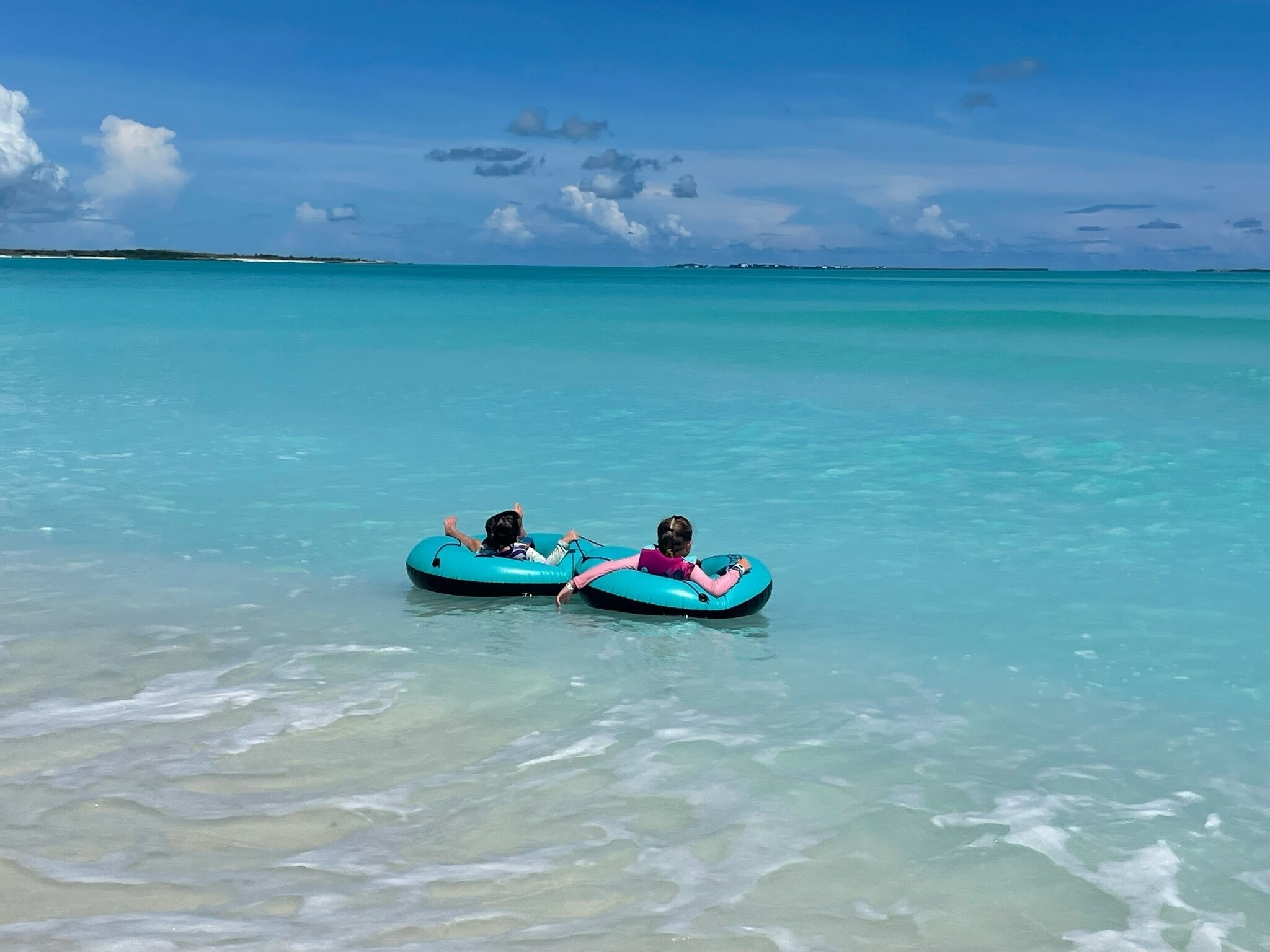 Two people floating on blue water tubes in a clear turquoise sea.
