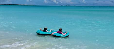 Two people floating on blue water tubes in a clear turquoise sea.