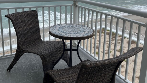 Ein Balkon mit Korbstühlen und einem Tisch, mit Blick auf einen Strand und den Ozean.