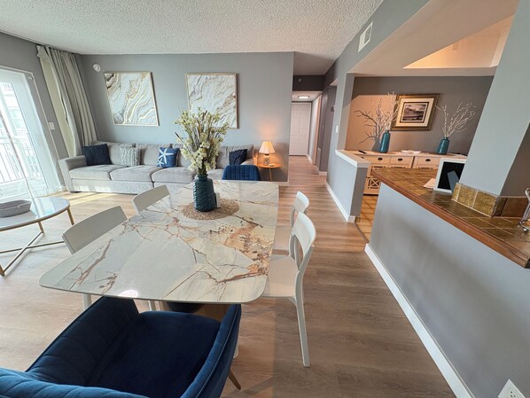 A modern living room with a dining table, sofas, and a kitchen area.