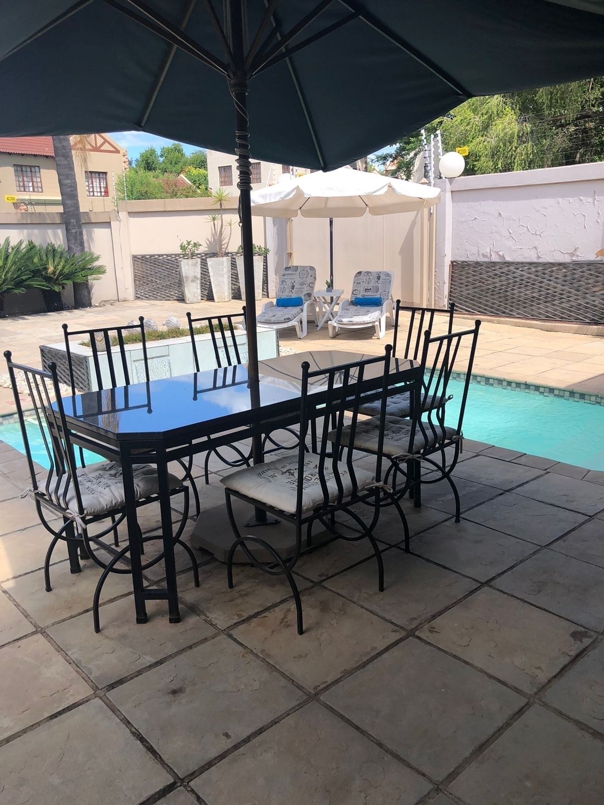 A poolside dining area with a table and chairs, a large umbrella, and lounge chairs.