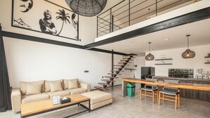Amplia sala de estar con sofá, mesa de centro y una escalera que lleva a una zona de cocina.