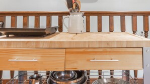 A kitchen with wooden countertops, a stainless steel rack for pots and pans, and a white mug with utensils.