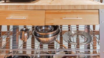 A kitchen with wooden countertops, a stainless steel rack for pots and pans, and a white mug with utensils.