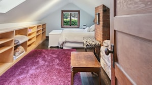 A cozy attic bedroom with a sloped ceiling, a skylight, a wooden door, a bed with a patterned headboard, a small table, and built-in shelves.