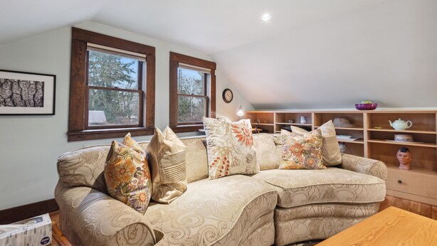 A cozy living room with a sofa, pillows, a wooden table, and a shelf with decorative items.