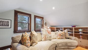 A cozy living room with a sofa, pillows, a wooden table, and a shelf with decorative items.