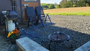 A small outdoor area with a grill, two lounge chairs, and a table. - Cozy modern farm Cabin. Enjoy the relaxing rural vibe just 40 minutes from CBD (Waitoki)
