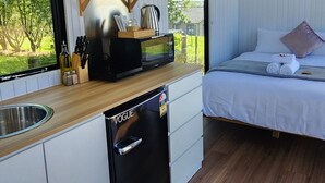 A compact room with a bed, a small kitchenette, and a window with a view of greenery. - Cozy modern farm Cabin. Enjoy the relaxing rural vibe just 40 minutes from CBD (Waitoki)