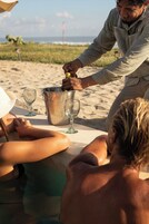Escena de playa con un balde de metal, una botella y dos vasos sobre una mesa.