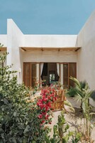 Un patio con un banco de madera, plantas en macetas y vistas del interior a través de una puerta de madera.