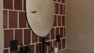 Une salle de bain avec un grand miroir, un lavabo et un luminaire fixé au mur.