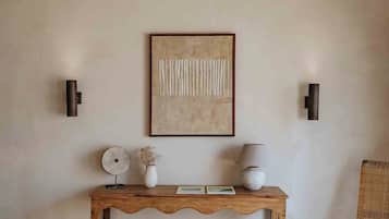 A bedroom with a bed, a wooden console table with decorative items, a wicker chair, and a ceiling with exposed beams.