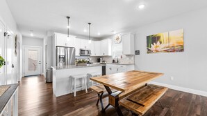 Una cocina moderna con armarios blancos, electrodomésticos de acero inoxidable y una mesa de comedor de madera.