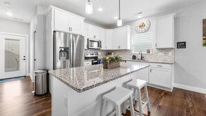 Una cocina moderna con armarios blancos, electrodomésticos de acero inoxidable, encimeras de granito y una isla central con taburetes de bar.