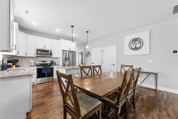 Una cocina moderna con armarios blancos, electrodomésticos de acero inoxidable y una mesa de comedor de madera con sillas.