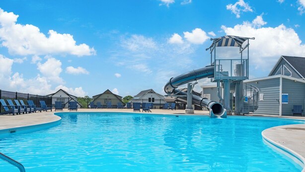 Une piscine avec un toboggan, des chaises longues et un poste de surveillance pour les sauveteurs.