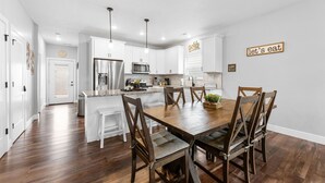A modern kitchen with white cabinets, a wooden dining table, and a 'Let's eat' sign. - Dog Friendly 3BR Lakeside Home with Indoor & Outdoor Pool Access (Hollister)