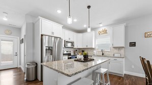 A modern kitchen with white cabinets, stainless steel appliances, and a granite island. - Dog Friendly 3BR Lakeside Home with Indoor & Outdoor Pool Access (Hollister)