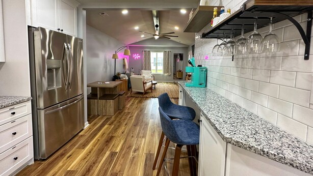 Une cuisine moderne dotée d’un réfrigérateur en acier inoxydable, de meubles en bois, d’un plan de travail en granit et d’un coin bar avec des tabourets.