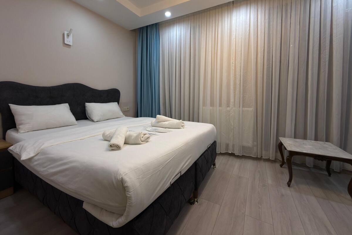 A neatly made bed with white linens and towels, a dark headboard, and a bedside table with a lamp.