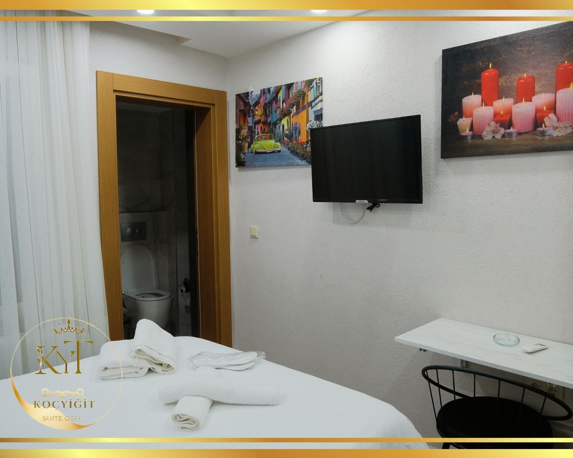 A hotel room with a bed, a TV mounted on the wall, a painting, and a small table with a chair.