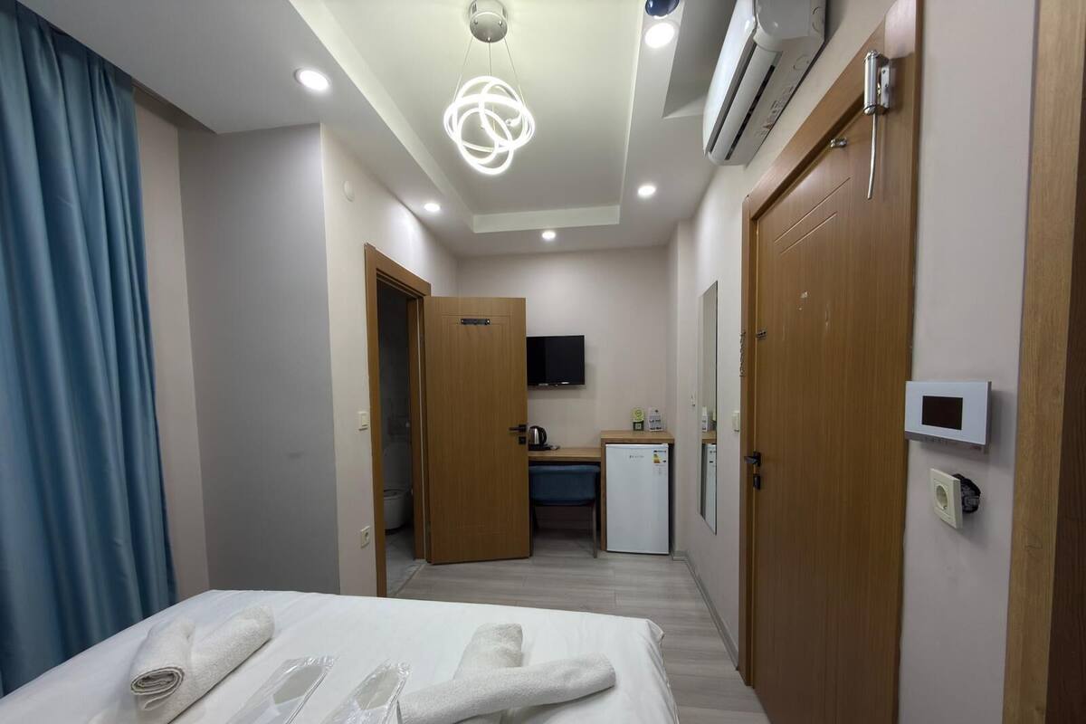 A hotel room with a bed, a desk, a small kitchenette, and a bathroom.
