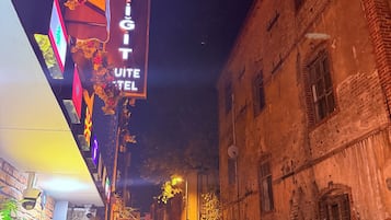 A narrow street with a sign for 'Kocis Hotel' and a building with a corrugated metal fence.