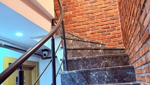 Un escalier avec des marches en marbre et un mur en briques, menant à une pièce dotée d’une porte en bois.