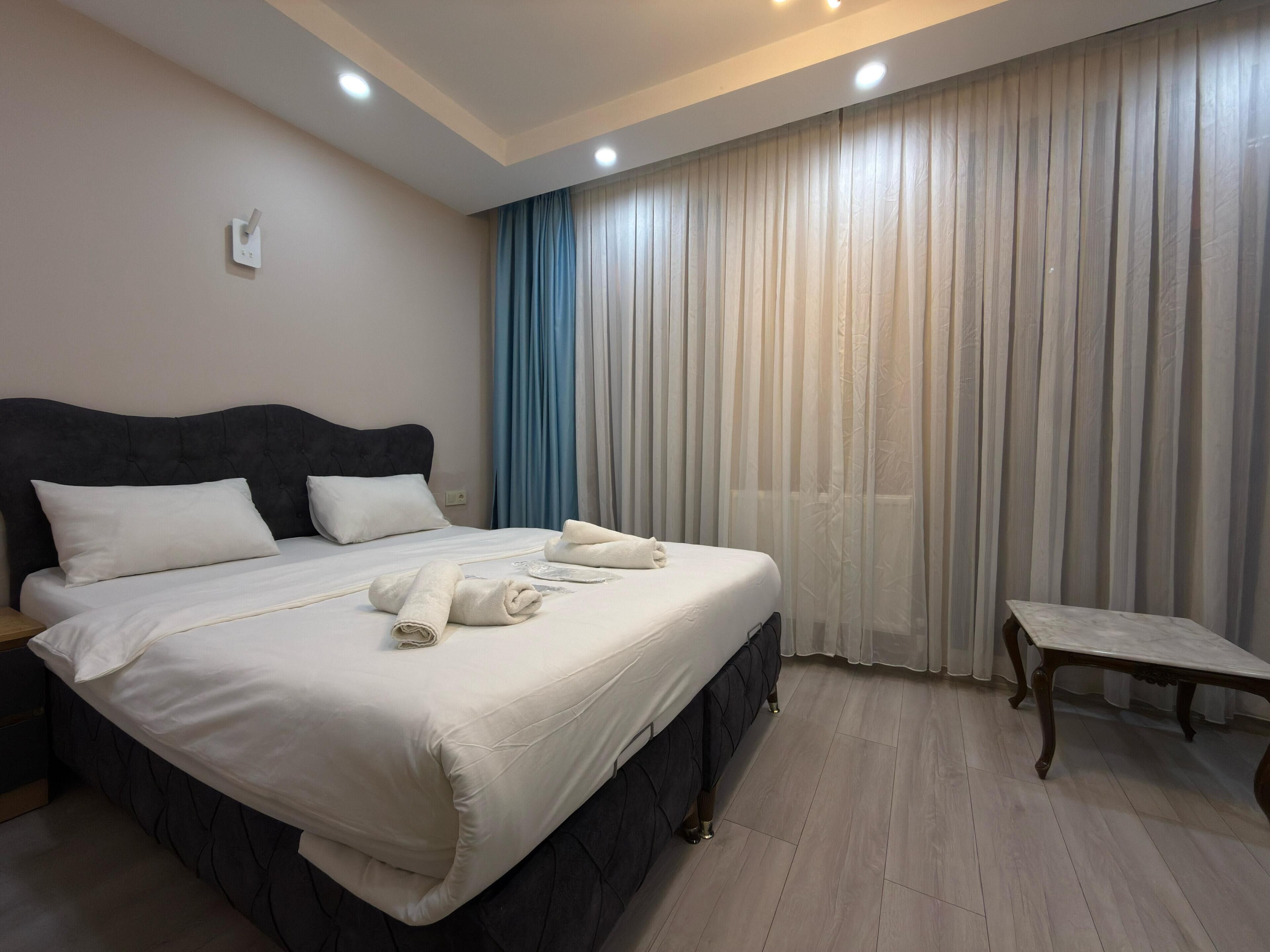 Una cama bien hecha con sábanas blancas, un cabecero oscuro y una mesita de noche con una lámpara.