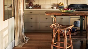Una cocina con armarios de madera, una mesa de comedor, sillas de mimbre y una lámpara colgante.