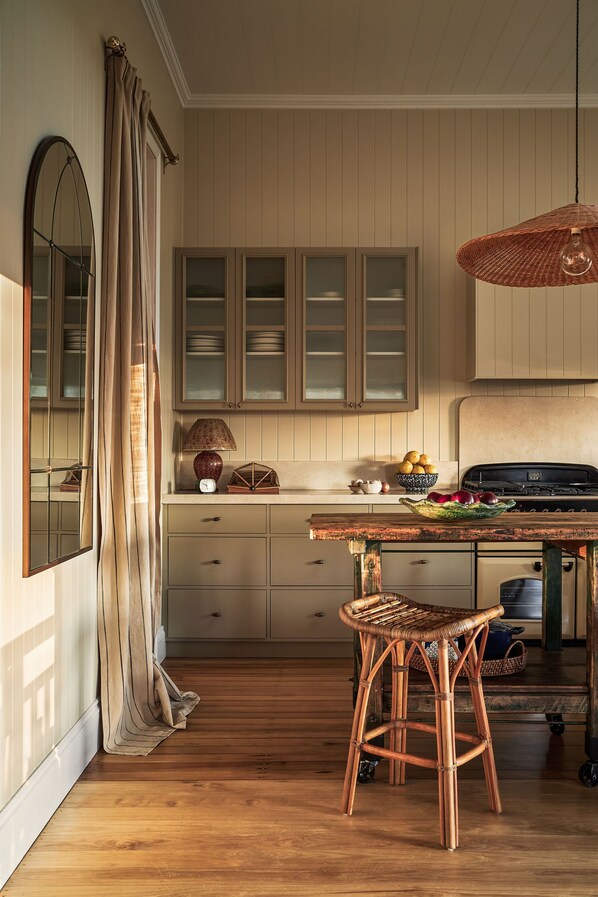 Una cocina con armarios de madera, una mesa de comedor, sillas de mimbre y una lámpara colgante.