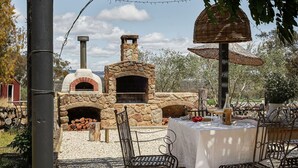 Un área de comedor al aire libre con un horno de pizza de piedra, una pérgola cubierta y una mesa lista para dos.