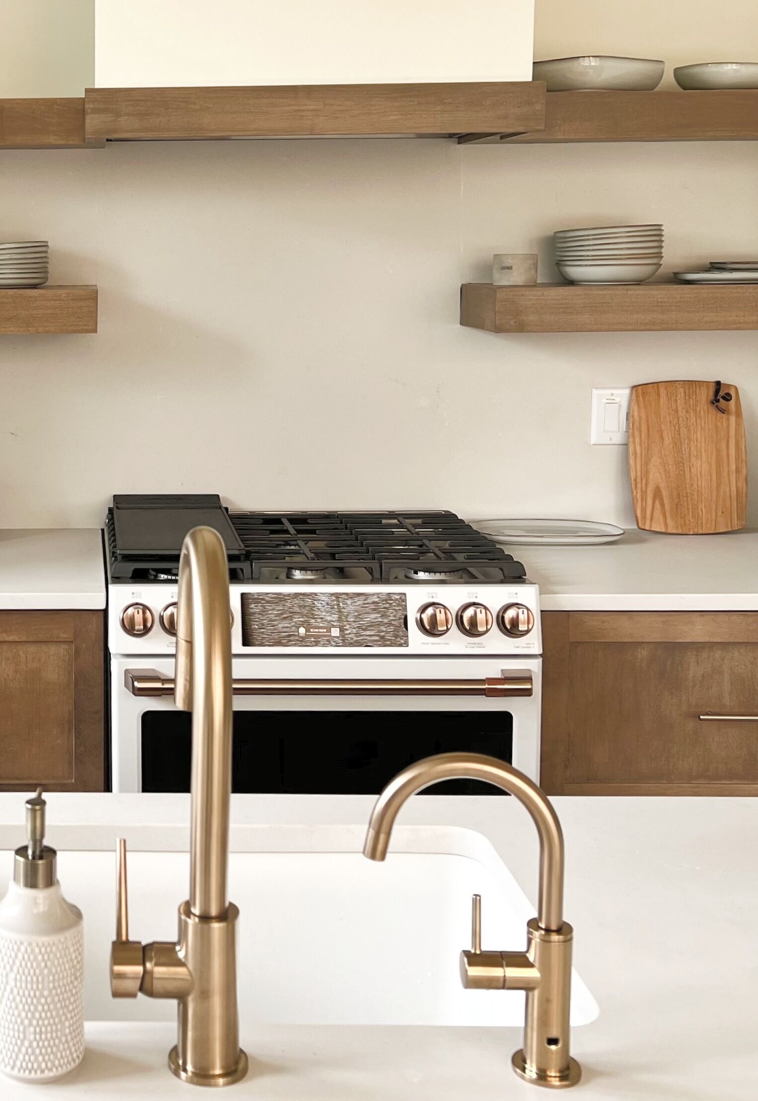 Cucina con piano cottura bianco, rubinetto in acciaio inossidabile ed mensole in legno.