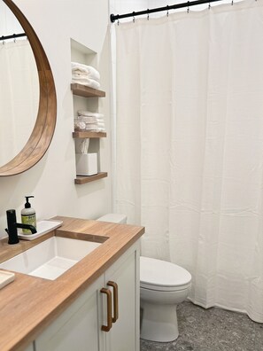 A modern bathroom with a wooden vanity, a round mirror, a toilet, and a shower curtain.