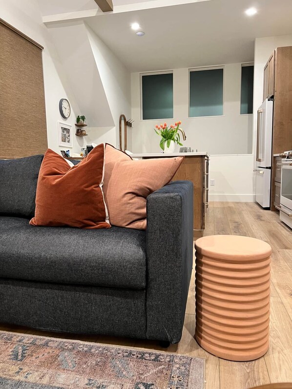 A modern living room with a grey sofa, a patterned rug, and a round ottoman.
