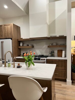 Eine moderne Küche mit Holzausstattung, einer weißen Arbeitsplatte, einem eingebauten Herd und einer Vase mit Blumen.