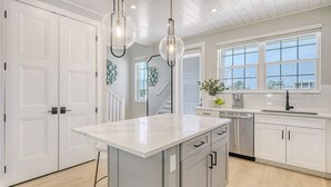 A modern kitchen with white cabinetry, a large island, stainless steel appliances, and a window with a view. - Saltwater Serenity | Canal Front w/ Heated Pool Near Anna Maria Island (Cortez)