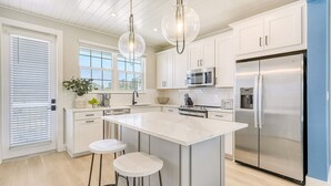 A modern kitchen with white cabinetry, a large island with stools, stainless steel appliances, and a hanging light fixture. - Saltwater Serenity | Canal Front w/ Heated Pool Near Anna Maria Island (Cortez)
