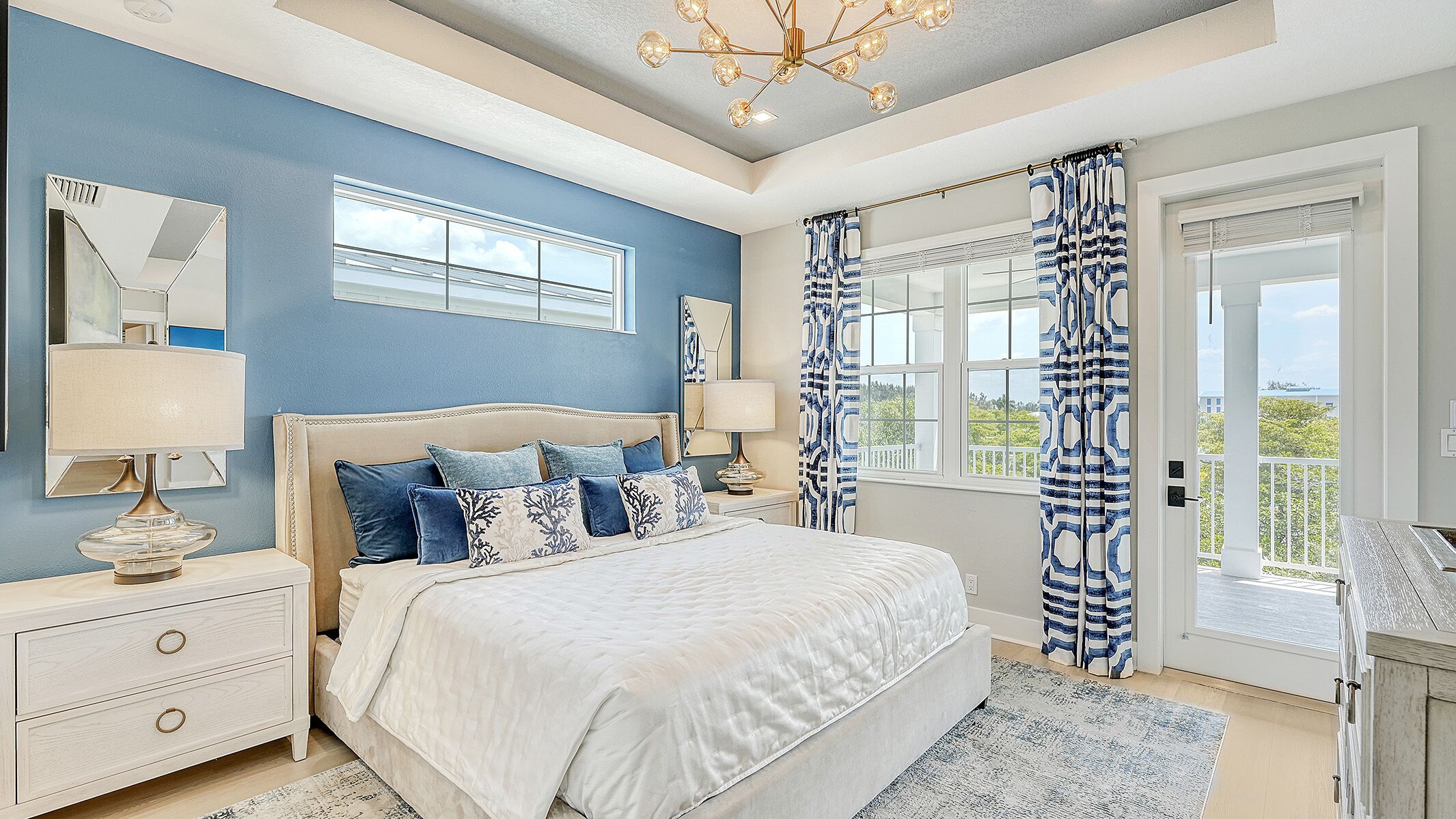 A bedroom with a large bed, bedside tables, a chandelier, and a view of the outdoors.