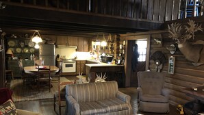 Ein gemütliches Blockhaus-Interieur mit Essbereich, Küche und Wohnzimmer, ausgestattet mit einer Couch, einem Sessel und einem runden Couchtisch.