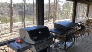 Ein Weber-Grill mit Propangasflaschen auf einer Holzterrasse mit Stühlen und einem Tisch.