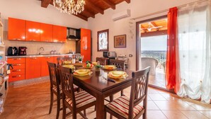 A dining area with a wooden table and chairs, a chandelier, and a kitchen with orange cabinets. - Sea view by Interhome (Muravera Villaputzu)