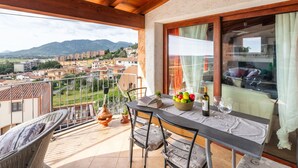 A balcony with a table set for dining, a wicker chair, and a view of a town and mountains. - Sea view by Interhome (Muravera Villaputzu)