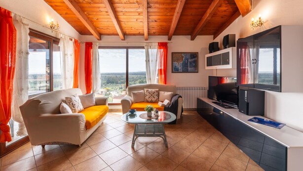 A spacious living area with a wooden ceiling, large windows, a sofa, a coffee table, and a kitchen area with a refrigerator and microwave. - Sea view by Interhome (Muravera Villaputzu)