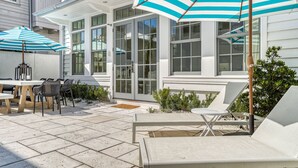 Eine Terrasse mit Außenbestuhlung, darunter ein Tisch und Stühle, und zwei gestreifte Sonnenschirme.