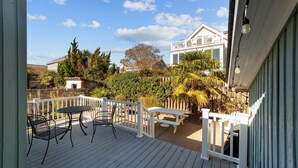 Una terraza de madera con una mesa y sillas, rodeada por una valla blanca y diversas plantas.
