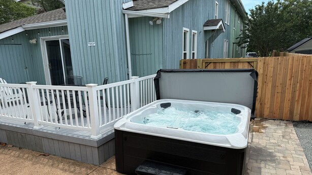 Un bain à remous avec des marches, une terrasse blanche et une maison en arrière-plan.