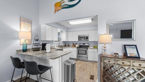 Una cocina moderna con armarios blancos, electrodomésticos de acero inoxidable y una isla central con taburetes de bar.